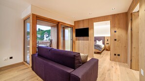Ein modernes Zimmer mit Holzboden, einem violetten Sofa, einem an der Wand befestigten Fernseher und einer Schiebetür zu einem Außenbereich.