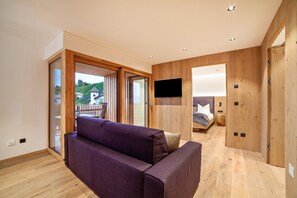 Una camera moderna con pavimento in legno, un divano viola, una TV a muro e una porta scorrevole in vetro che dà su una zona esterna.