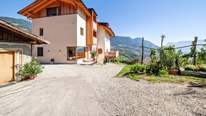 A two-story building with a wooden facade, a gravel driveway, and a mountain backdrop. - Apartment 'Huetterhof Langes' with Mountain View, Private Terrace and Wi-Fi (Caines)