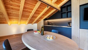 A modern kitchen with wooden beams, a dining table with chairs, and a fruit bowl.