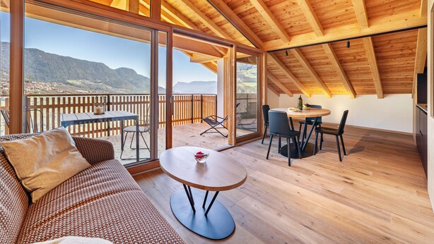 A spacious room with a wooden ceiling, large sliding glass doors, a round table, and a sofa.