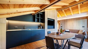 A modern kitchen with dark cabinetry, a wooden dining table, and a built-in TV.