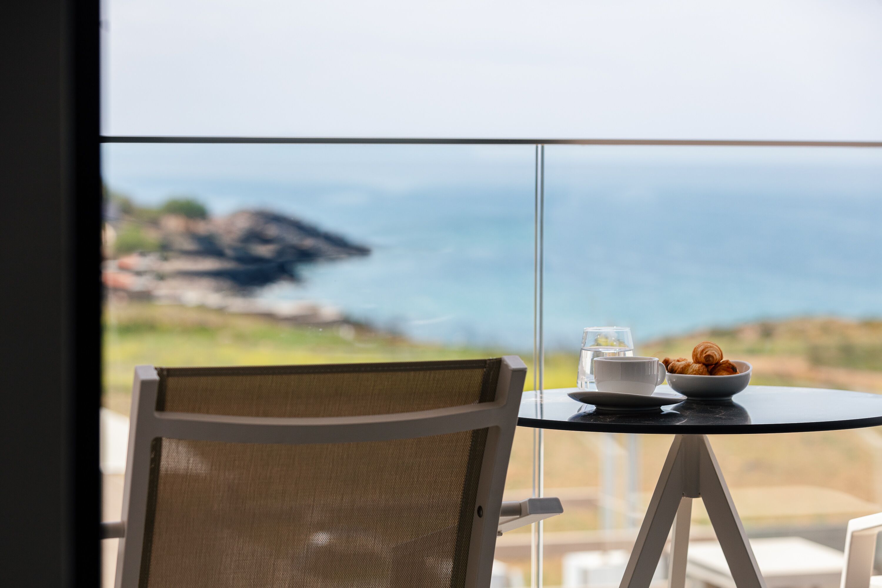 A dining table with a bowl of pastries and a cup, overlooking a scenic coastal view.