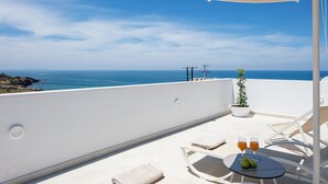 Ein Balkon mit Meerblick, ein Tisch mit Gläsern und Früchten sowie eine Topfpflanze.