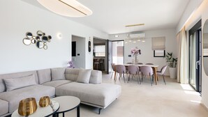 Ein modernes Wohnzimmer mit einem Ecksofa, einem Essbereich mit Tisch und Stühlen sowie einem großen Fenster mit Vorhängen.