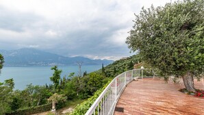 A wooden deck with a white railing, overlooking a body of water and mountains. - Apartment 'Villa Verde' with Lake View, Shared Pool and Air Conditioning (Torri del Benaco)