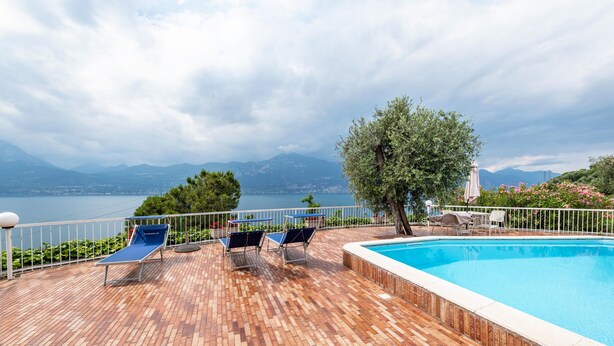 A poolside area with lounge chairs, a swimming pool, and a view of the sea and mountains. - Apartment 'Villa Verde' with Lake View, Shared Pool and Air Conditioning (Torri del Benaco)