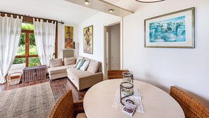 A cozy living room with a sofa, wicker chairs, a round table with candles, and artwork on the walls. - Apartment 'Villa Verde' with Lake View, Shared Pool and Air Conditioning (Torri del Benaco)