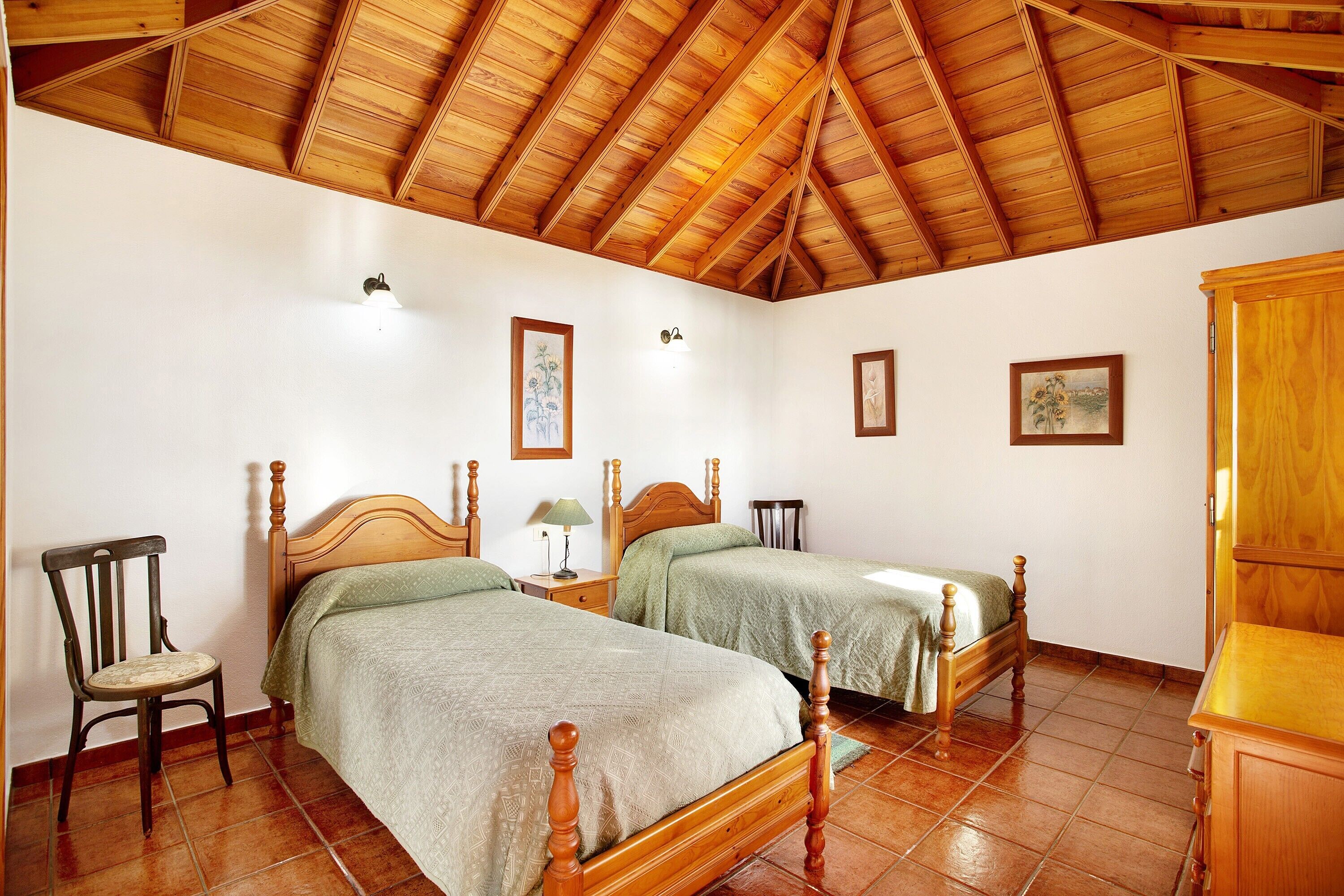 Quarto com duas camas de madeira, uma cadeira, um armário e piso de azulejos.