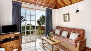 Una sala de estar con televisor, sofá, mesa de centro y puerta corrediza de vidrio que da a un jardín.