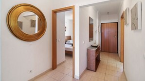 Un passadís amb un mirall rodó, una porta de fusta i un llit al fons.