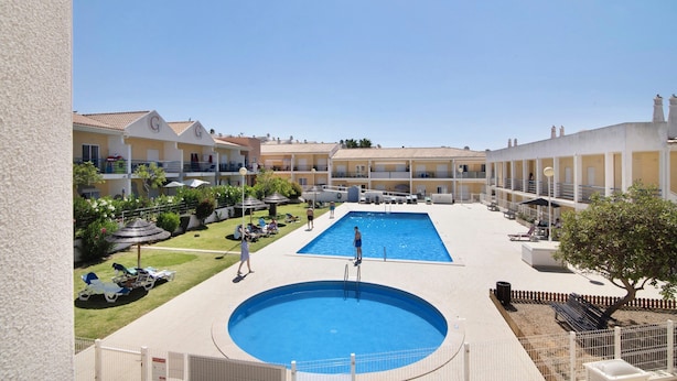 Un hotel amb piscina central, gandules i una zona de terrassa amb tanca.