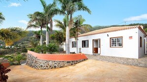 A white building with a tiled roof, a stone wall, and a paved patio area. - Holiday Home 'Casa Ariadna' with Sea Views, Private Garden, and Wi-Fi (Tijarafe)