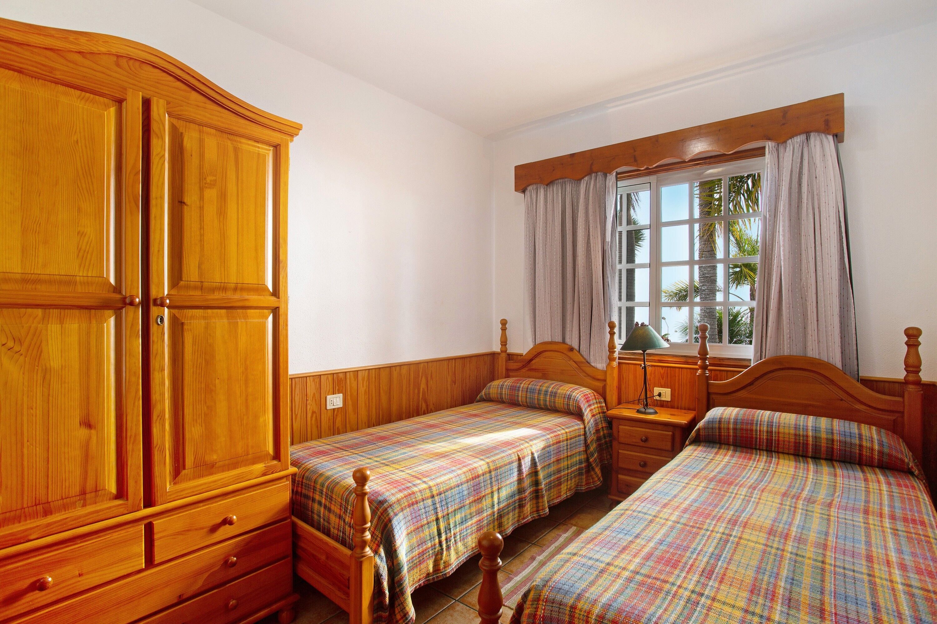 A bedroom with two single beds, wooden wardrobe, and a window with curtains.