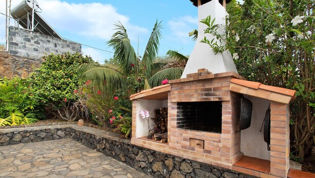 A stone patio with a brick barbecue area surrounded by lush greenery. - Holiday Home 'Casa Ariadna' with Sea Views, Private Garden, and Wi-Fi (Tijarafe)