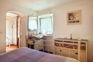 Een slaapkamer met een bed, een kaptafel met spiegel, een raam met gordijnen, en een aan de muur hangend schilderij.