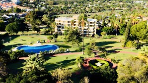 A residential area with a swimming pool, green lawns, and a multi-story building.