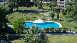A swimming pool surrounded by grass, trees, and a multi-story building.