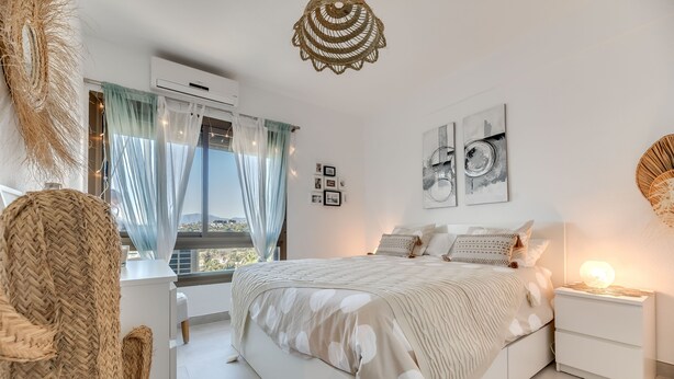 A bedroom with a bed, bedside tables, a window with curtains, wall art, and a hanging light fixture.