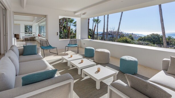 A modern outdoor living area with a sofa, chairs, and tables, overlooking a scenic view of the ocean and palm trees. - Villa 'Nagueles' with Sea View, Wi-Fi and Air Conditioning (Marbella)