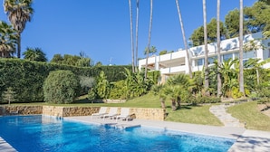 A swimming pool with lounge chairs, surrounded by palm trees and a white building with large windows. - Villa 'Nagueles' with Sea View, Wi-Fi and Air Conditioning (Marbella)