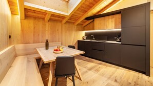 Eine moderne Küche mit Holzbalken und einem Oberlicht, ein Essbereich mit Tisch und Stühlen sowie einer schwarzen Arbeitsplatte.