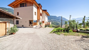 Ein zweistöckiges Gebäude mit Holzfassade, einem Schotterweg und Bergen im Hintergrund.