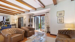 Ein Wohnzimmer mit zwei Ledersofas, einem Glastisch, Holzbalken an der Decke und Blick durch eine Glastür.