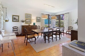 Un espace repas comprenant une table, des chaises, un buffet et donnant sur l’extérieur.