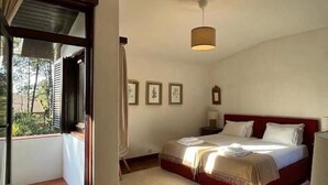 Ein Schlafzimmer mit einem Bett, einem Nachttisch, einer Pendelleuchte und einem Fenster mit Vorhängen.