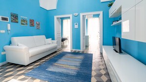 Una sala de estar con un sofá blanco, un tapete azul y un televisor sobre un mueble blanco.