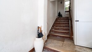 Una escalera que lleva a una puerta, un jarrón blanco con un paraguas y un pequeño árbol de Navidad.