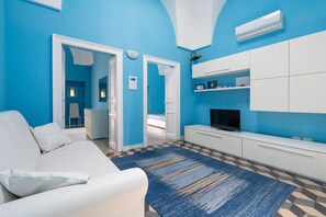 Un salon moderne avec un mur d’accent bleu, un canapé blanc, un téléviseur et un tapis à motifs.