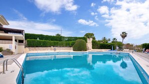 Una piscina con agua cristalina azul, rodeada por un muro de piedra, y un edificio con un balcón a la izquierda.