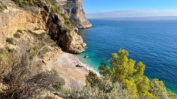 Un paisaje costero con acantilados rocosos, una playa y mar azul cristalino.