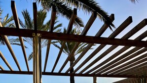 Una pérgola de madera con un banco, con vistas a una zona costera con palmeras y el océano.