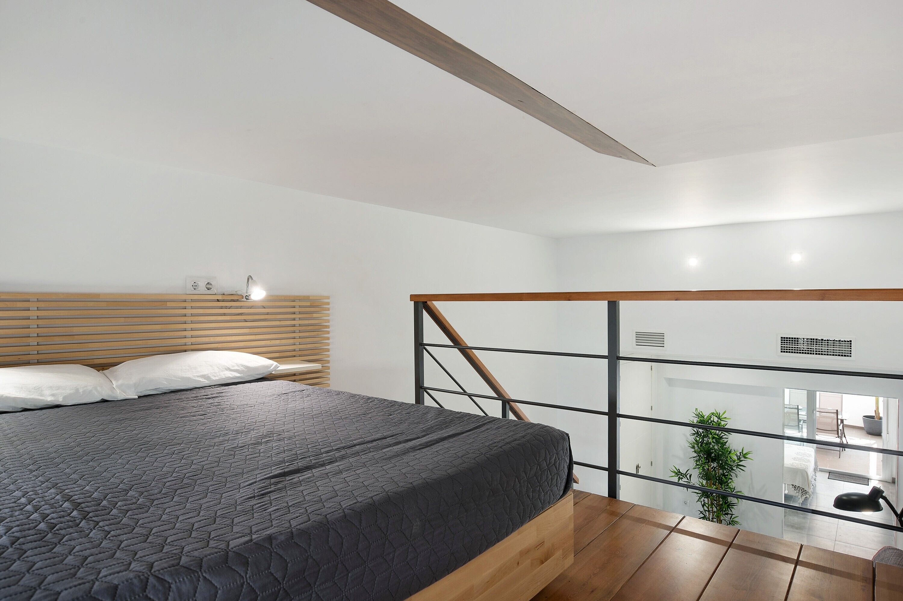 Un dormitorio moderno con una cama grande, cabecera de madera y vista al área de estar a través de un separador de vidrio.