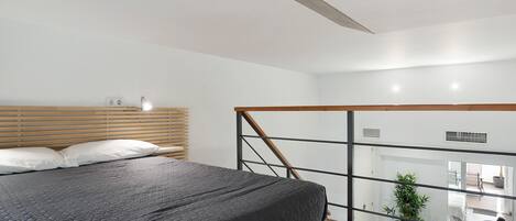 Un dormitorio moderno con una cama grande, cabecera de madera y vista al área de estar a través de un separador de vidrio.