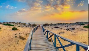 Un muelle de madera que conduce a una playa con un atardecer de fondo.