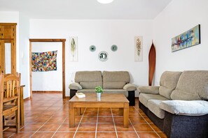 Een woonkamer met een houten salontafel, twee banken, een houten stoel en een kleurrijke wandtapijt.