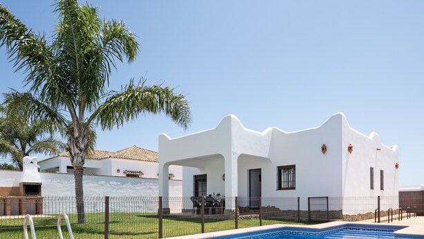 A white building with a pool, palm trees, and a clear sky. - Holiday Home 'Villa Cala Salada' with Private Pool, Wi-Fi and Air Conditioning (Conil de la Frontera)