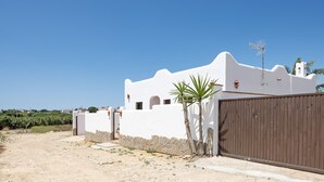 A white building with a brown gate, a stone wall, and a palm tree. - Holiday Home 'Villa Cala Salada' with Private Pool, Wi-Fi and Air Conditioning (Conil de la Frontera)