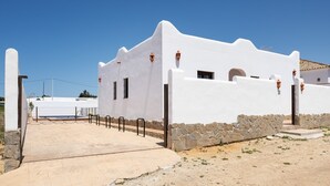 A white building with a stone base, a paved entrance, and a clear blue sky. - Holiday Home 'Villa Cala Salada' with Private Pool, Wi-Fi and Air Conditioning (Conil de la Frontera)