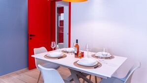A dining area with a white table set for four, a red door, and a black pendant light.