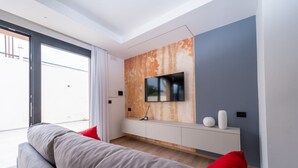 A modern living room with a grey sofa, red cushions, a TV mounted on a textured wall, and a white console table.