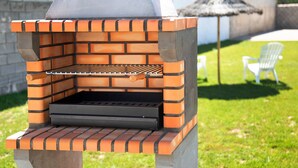 Un barbecue extérieur en briques, doté d’une cheminée, d’une grille en métal et d’un panneau de commande.