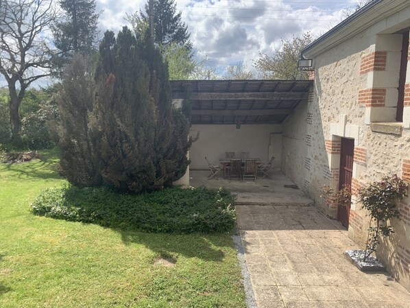 A covered patio area with a table and chairs, surrounded by a brick wall and a large tree.