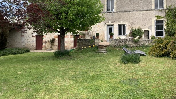 Une maison en pierre avec un jardin, un arbre et une pelouse.