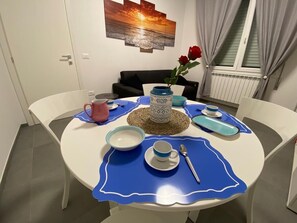 A dining table set with blue placemats, white plates, and a blue and white vase with red roses.