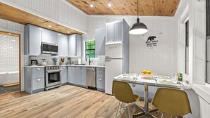 A modern kitchen with grey cabinets, a stainless steel refrigerator, and a dining area with two chairs and a table set for two.